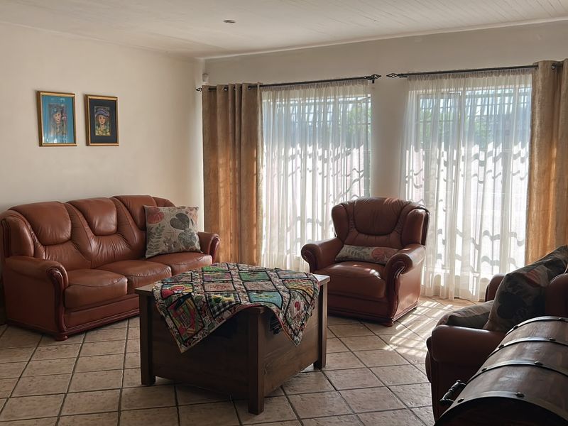 A spacious living room featuring neutral tiled flooring, recessed ceiling lighting, and large windows that allow for ample natural light.
