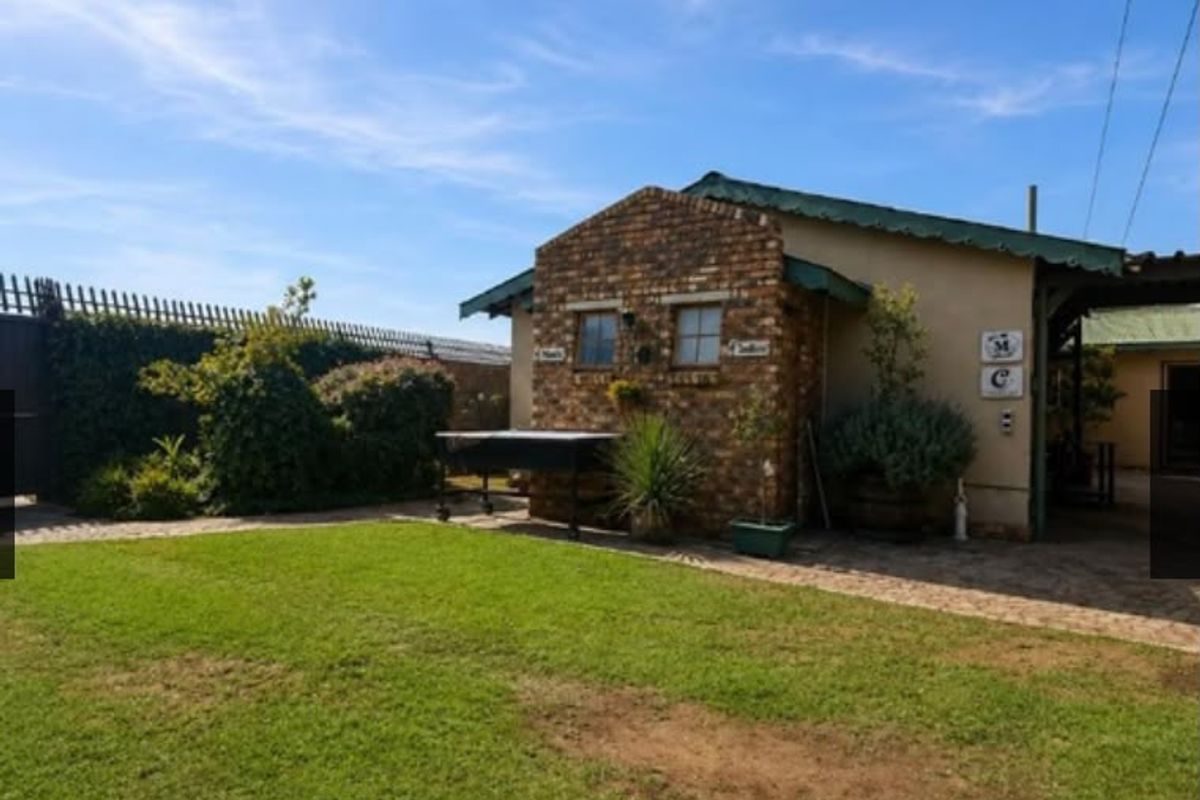 A rear view of the property featuring a brick facade, metal roofing, a paved patio area, and a well-maintained lawn.