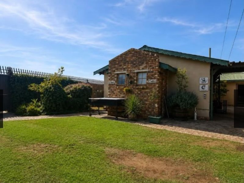 A rear view of the property featuring a brick facade, metal roofing, a paved patio area, and a well-maintained lawn.