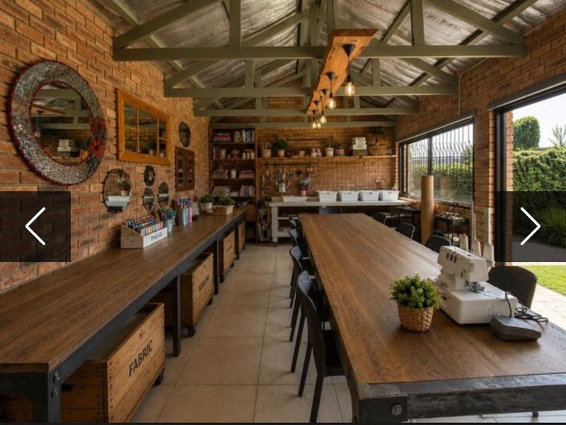 A spacious, well-lit utility or craft room featuring exposed brick walls, timber roof trusses, built-in workbenches, and large sliding doors opening to the garden.