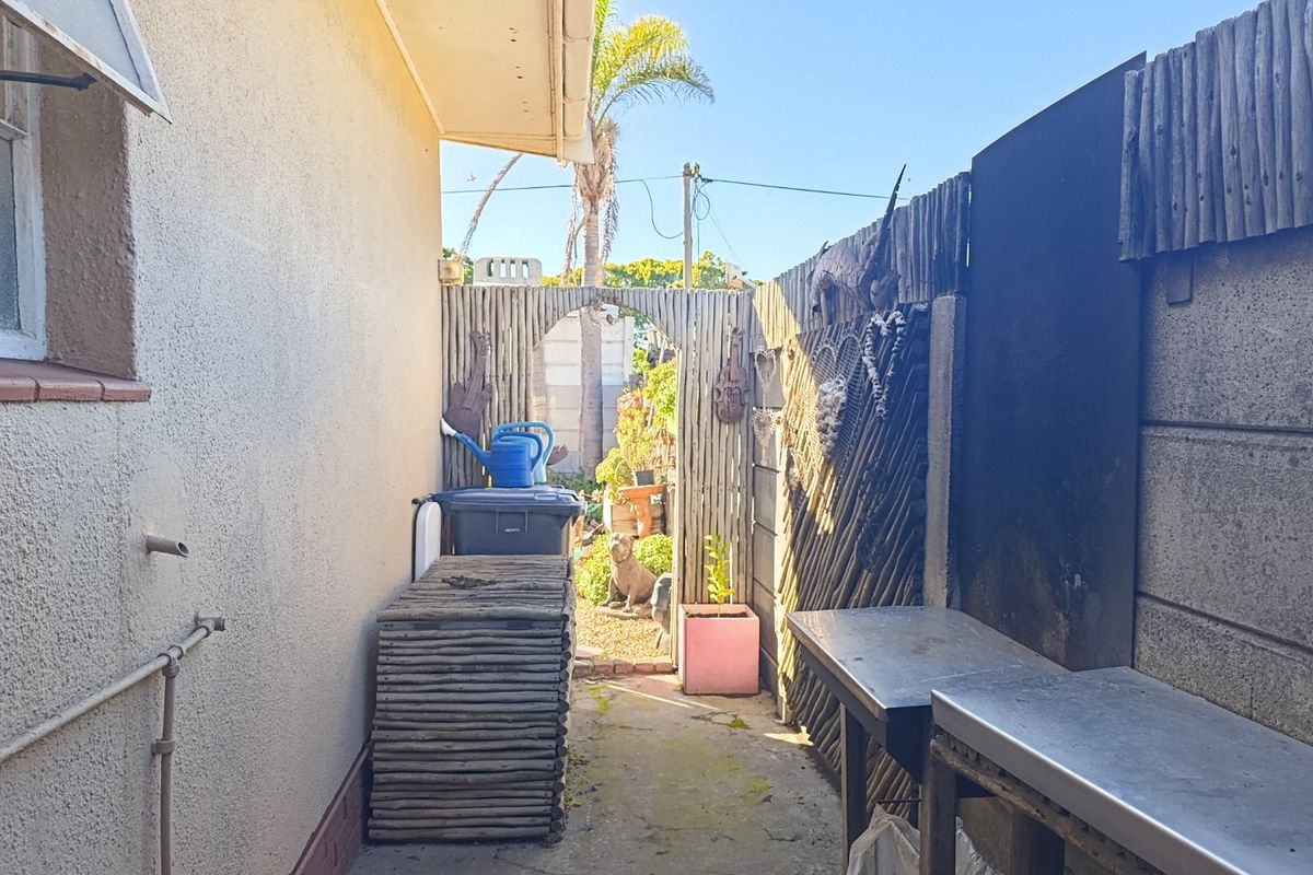 A narrow rear exterior side passage featuring concrete paving, a metal prep station, and timber screening, providing functional outdoor utility space.