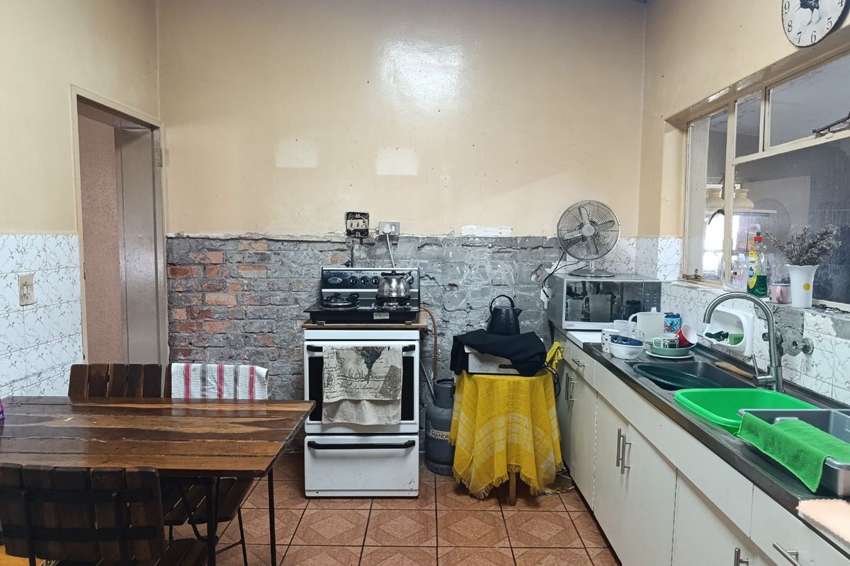A functional kitchen featuring tiled flooring, a stainless steel sink, and a freestanding stove, currently requiring wall finishing and cosmetic updates.
