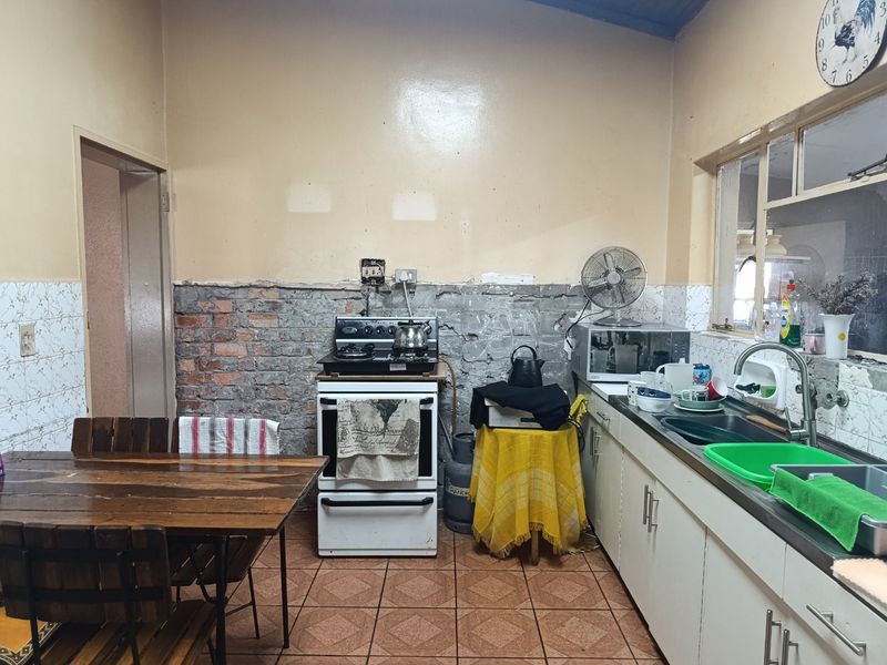 A functional kitchen featuring tiled flooring, a stainless steel sink, and a freestanding stove, currently requiring wall finishing and cosmetic updates.