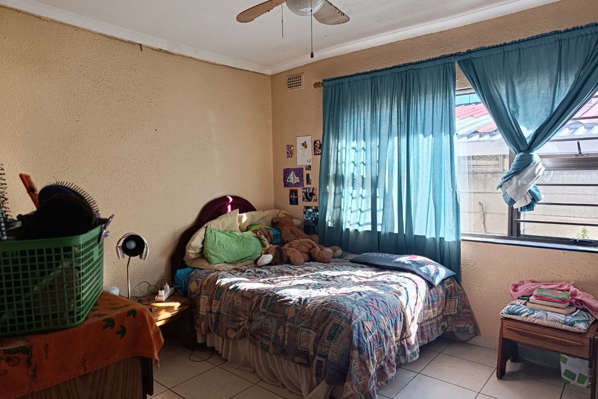 A bedroom featuring tiled flooring and a ceiling fan, with natural light entering through a window with curtains.