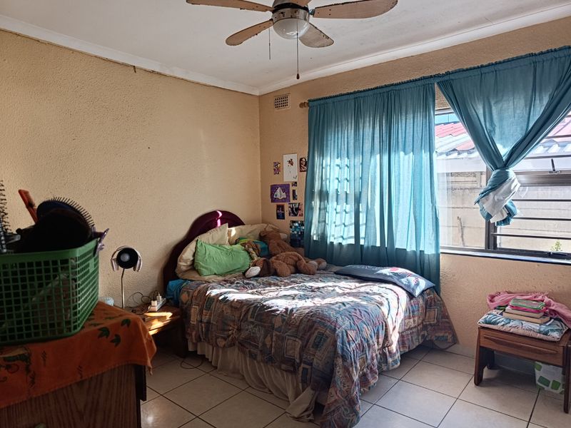 A bedroom featuring tiled flooring and a ceiling fan, with natural light entering through a window with curtains.