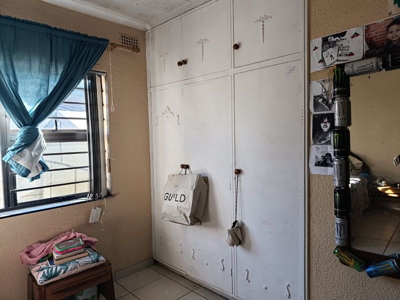Bedroom featuring built-in cupboards, tiled flooring, and security bars on the window. The room requires cosmetic updates to improve its overall condition.