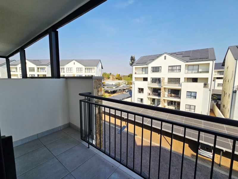 A clean, modern balcony featuring tiled flooring, a secure metal balustrade, and a stone-clad pillar, offering an elevated view of the apartment complex.