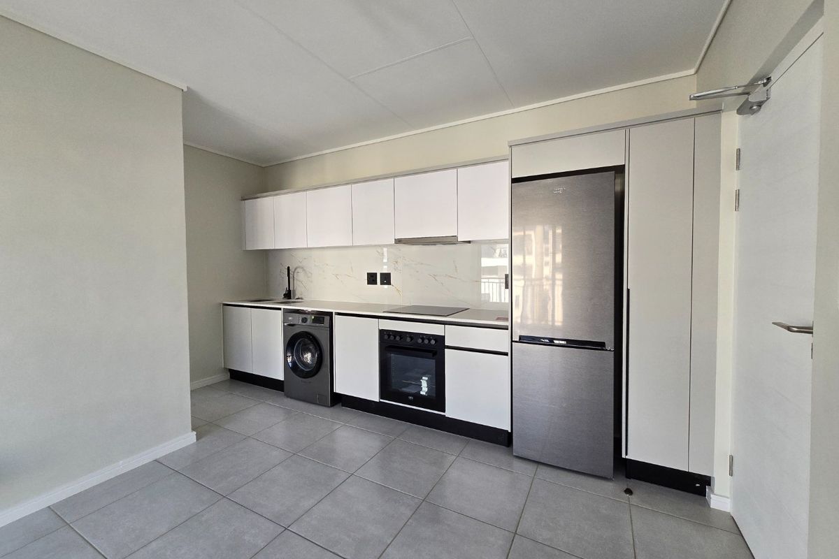 Modern kitchen featuring sleek white cabinetry, integrated appliances, marble-look splashback, and neutral tiled flooring in a clean, minimalist layout.