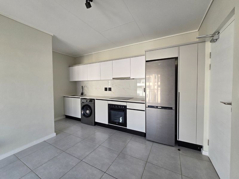 Modern kitchen featuring sleek white cabinetry, integrated appliances, marble-look splashback, and neutral tiled flooring in a clean, minimalist layout.