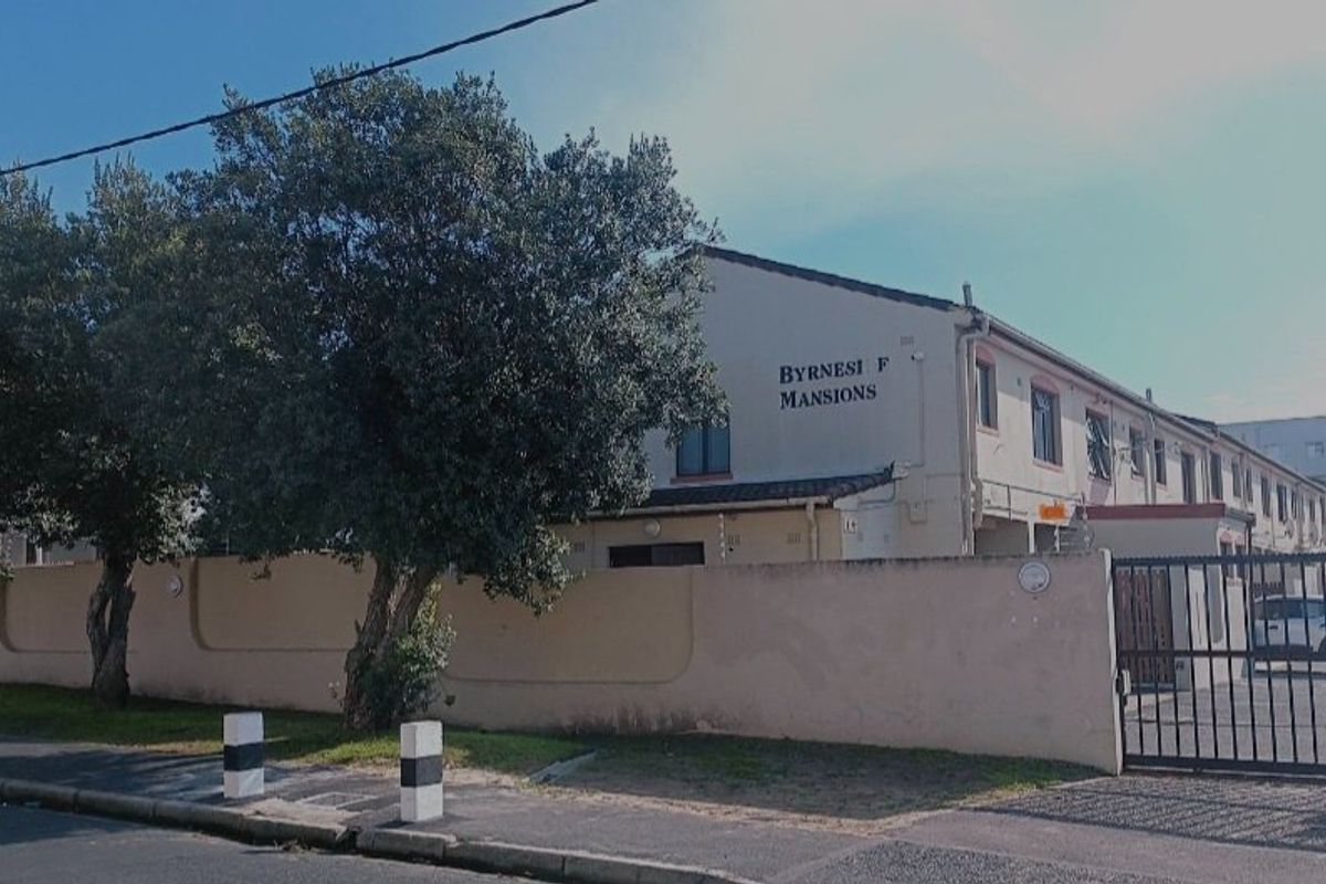 Street view of Byrnesi F Mansions apartment complex featuring a perimeter wall, electric fencing, and gated driveway access.