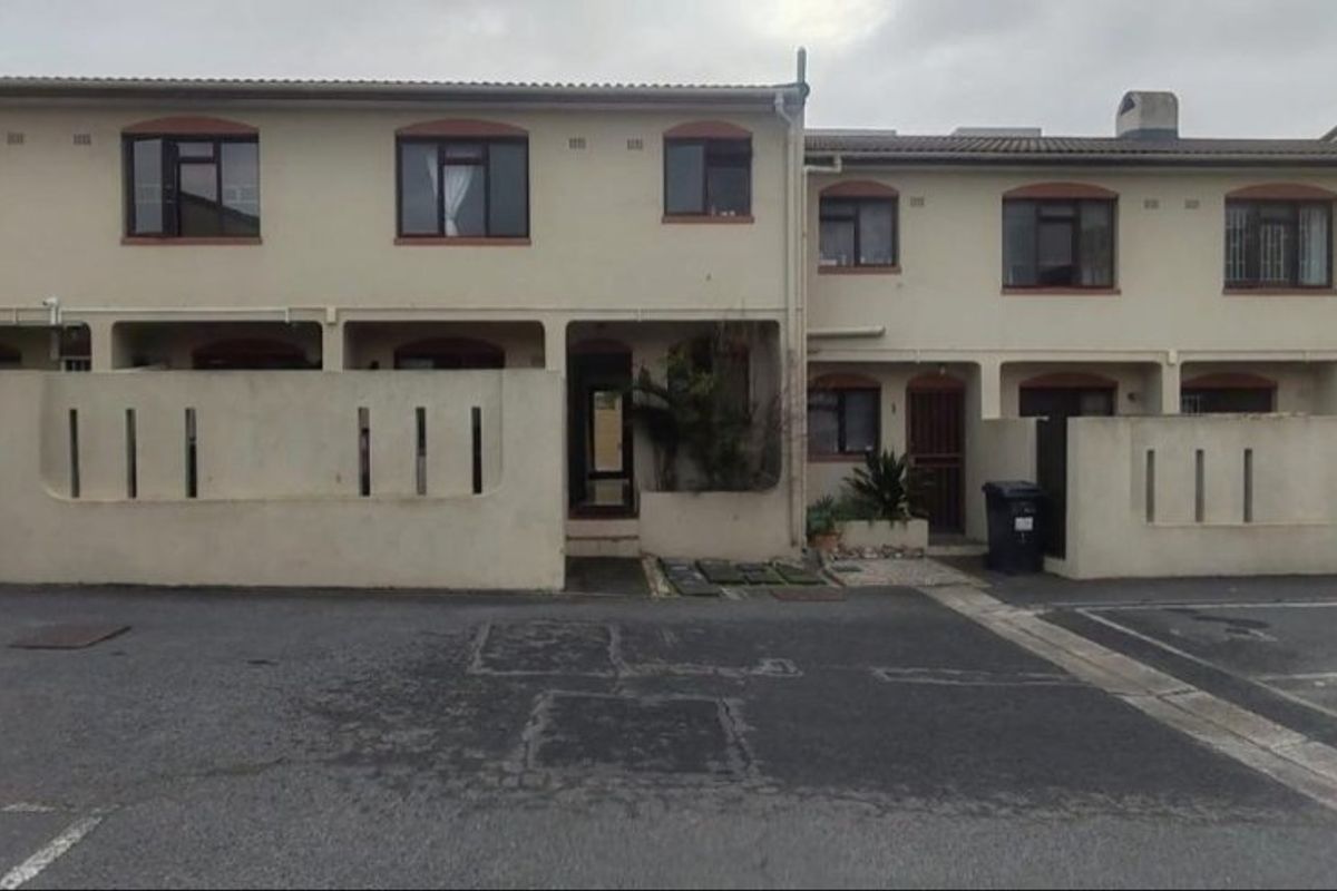 Front elevation of a low-rise apartment complex featuring concrete boundary walls, paved driveway access, and standard window configurations.