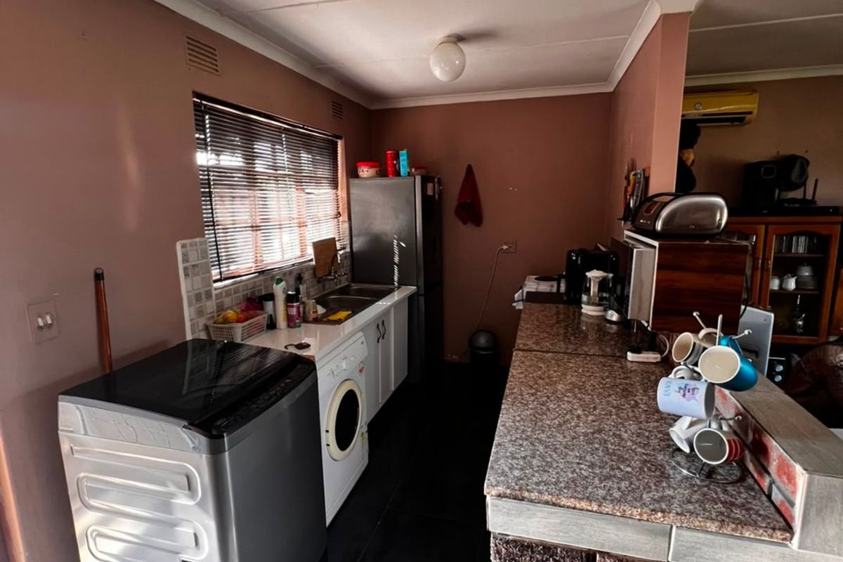 A functional kitchen featuring a brick breakfast bar, granite countertops, and tiled flooring, offering a practical layout with integrated sink and cabinetry.