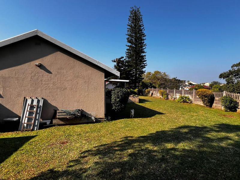 A view of the rear exterior of the house featuring a large lawn and a concrete boundary wall.