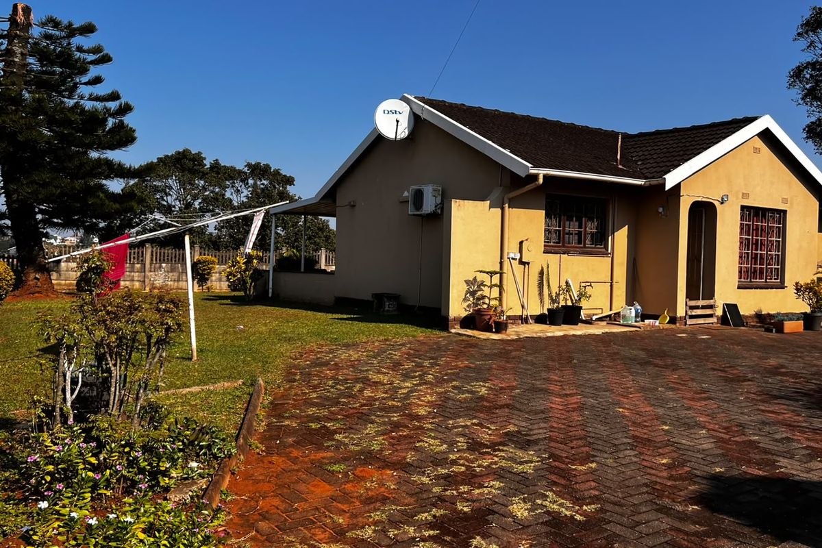Rear view of the house featuring a paved driveway, landscaped garden, and exterior wall finishes with an installed satellite dish and air conditioning unit.