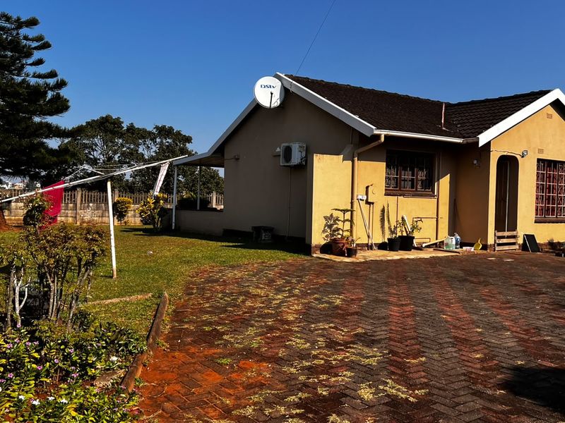 Rear view of the house featuring a paved driveway, landscaped garden, and exterior wall finishes with an installed satellite dish and air conditioning unit.