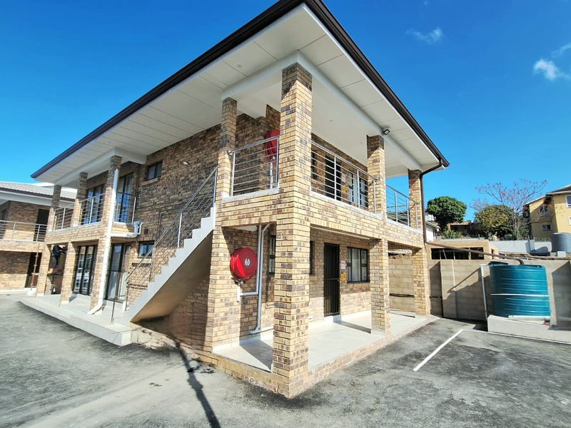 A multi-story townhouse exterior featuring face brick construction, covered patios, balconies with stainless steel balustrades, and an external staircase.