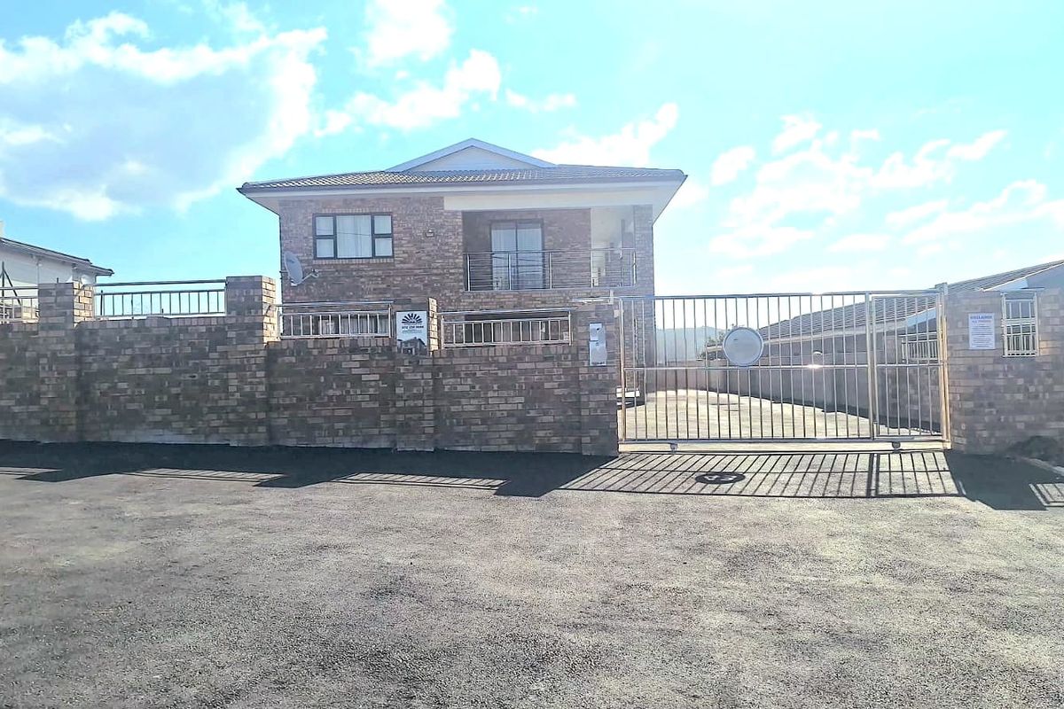 Front elevation of a double-story townhouse featuring a face brick facade, secure metal gate, and paved driveway access.