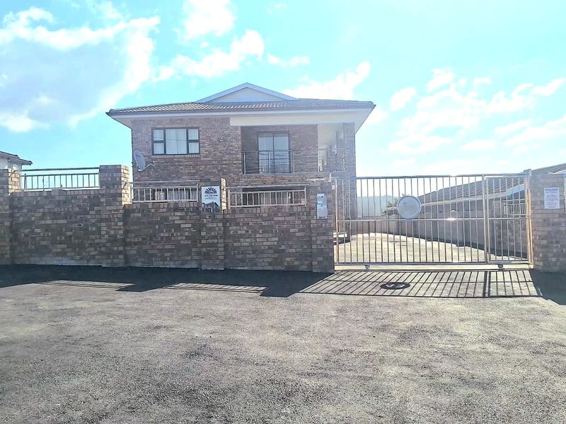 Front elevation of a double-story townhouse featuring a face brick facade, secure metal gate, and paved driveway access.