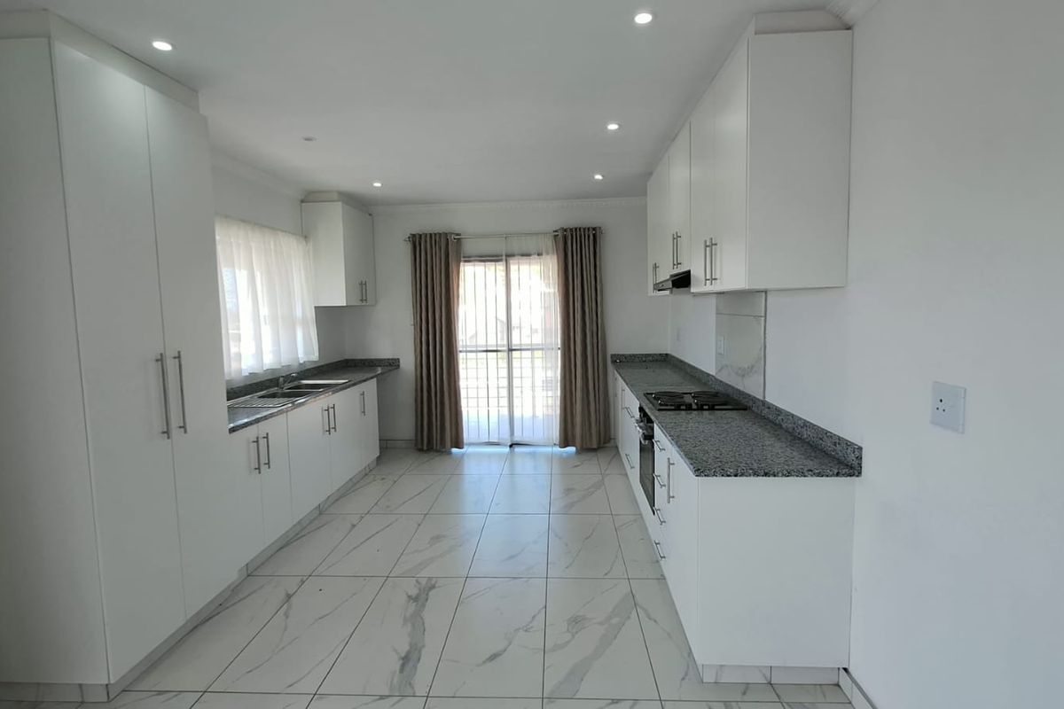 Modern kitchen featuring white cabinetry, granite countertops, built-in oven, gas hob, and tiled flooring with direct access to the exterior.