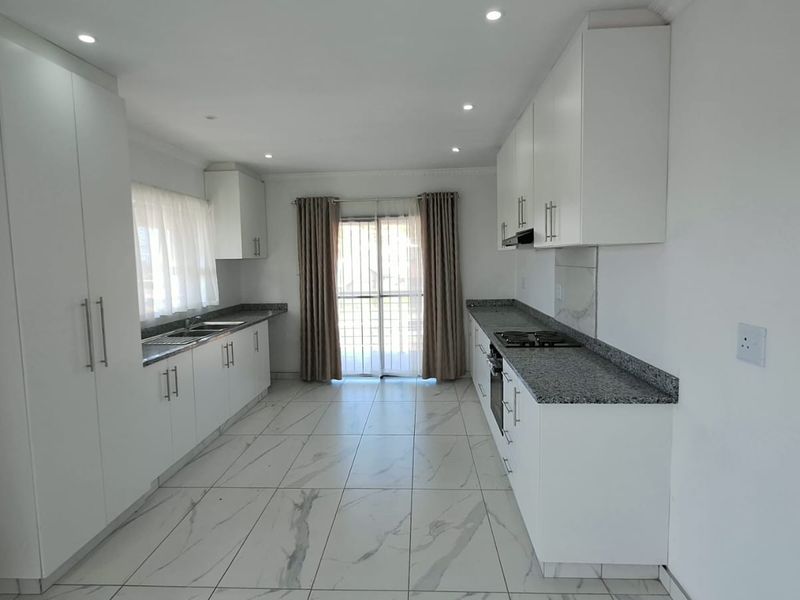 Modern kitchen featuring white cabinetry, granite countertops, built-in oven, gas hob, and tiled flooring with direct access to the exterior.
