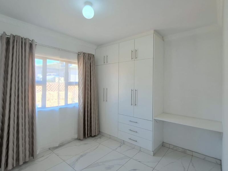 A bright bedroom featuring modern white built-in wardrobes, a built-in desk, and clean tiled flooring.