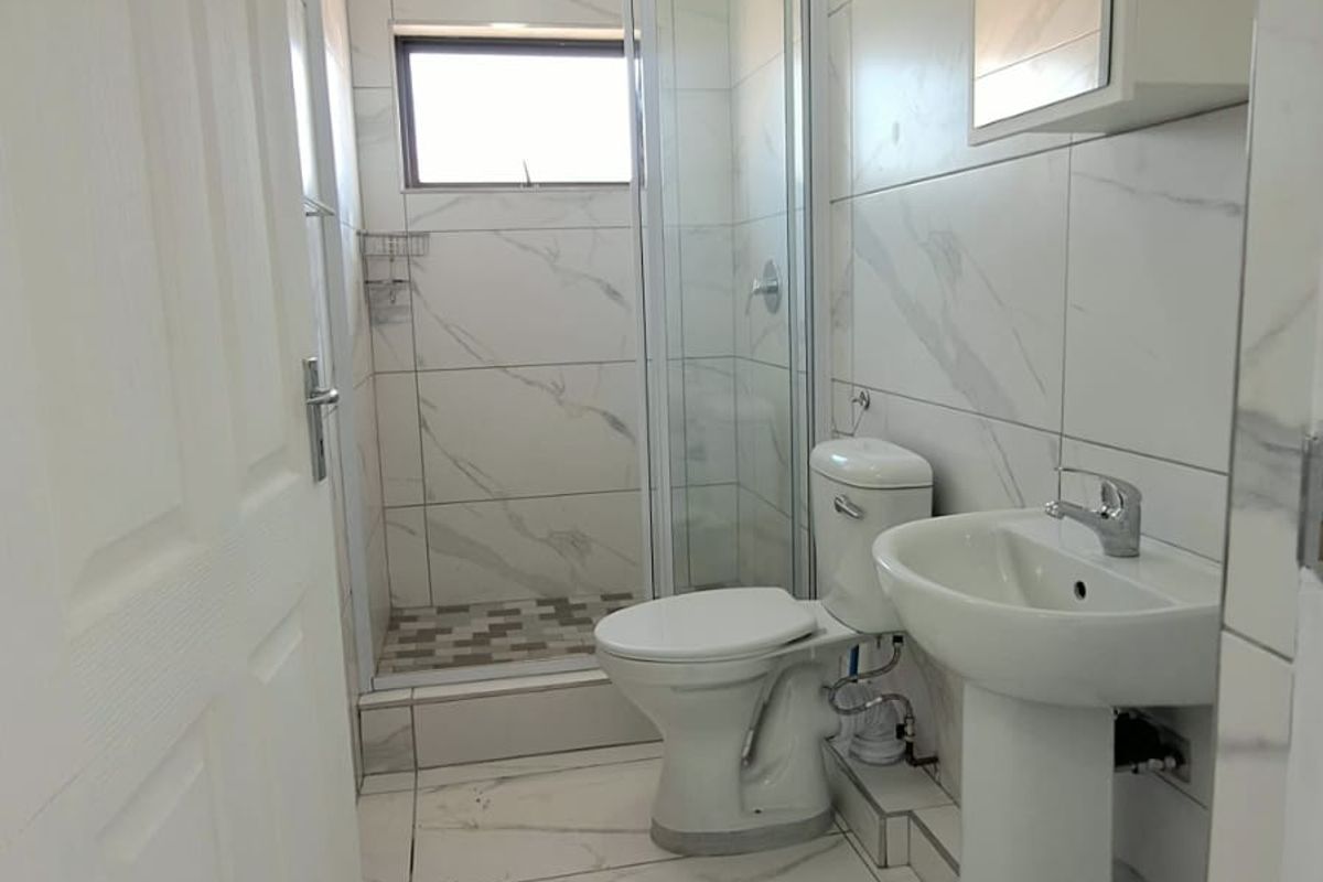 A compact bathroom featuring marble-look tiling, a pedestal basin, a toilet, and a glass-enclosed shower unit.