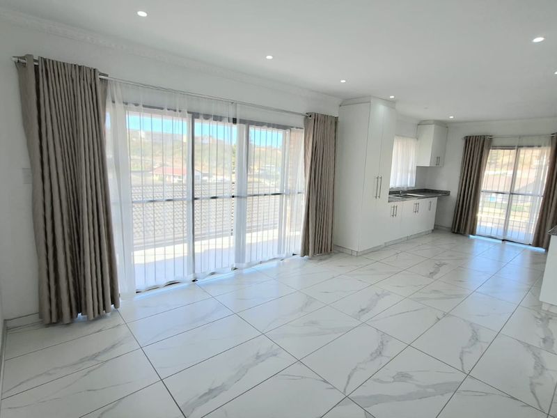 Spacious open-plan living and kitchen area featuring modern marble-look floor tiles, recessed lighting, and large sliding doors leading to an outdoor balcony.