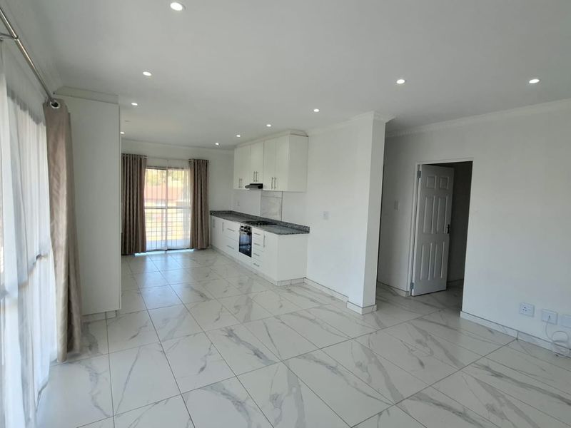 Bright open-plan living area featuring modern marble-look floor tiles, recessed lighting, and a sleek kitchen with granite countertops and built-in appliances.