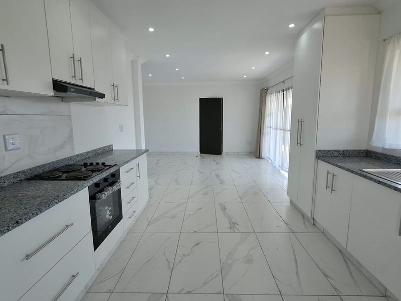 Modern open-plan kitchen featuring white cabinetry, granite countertops, integrated appliances, and sleek porcelain floor tiles, flowing into a spacious living area.