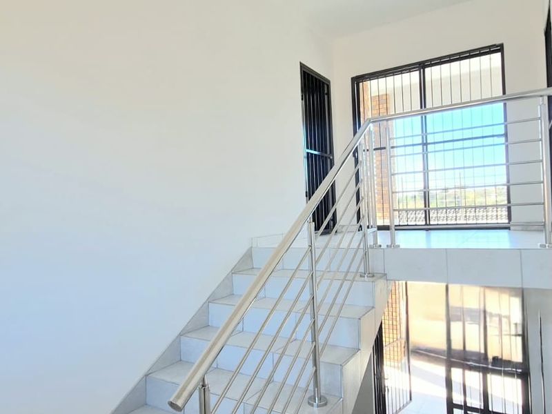 Bright and spacious hallway featuring a tiled staircase with a modern stainless steel balustrade and secure access points.
