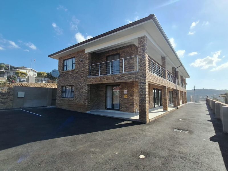 A modern double-story townhouse featuring a face-brick exterior, covered balconies, and a spacious paved driveway area.