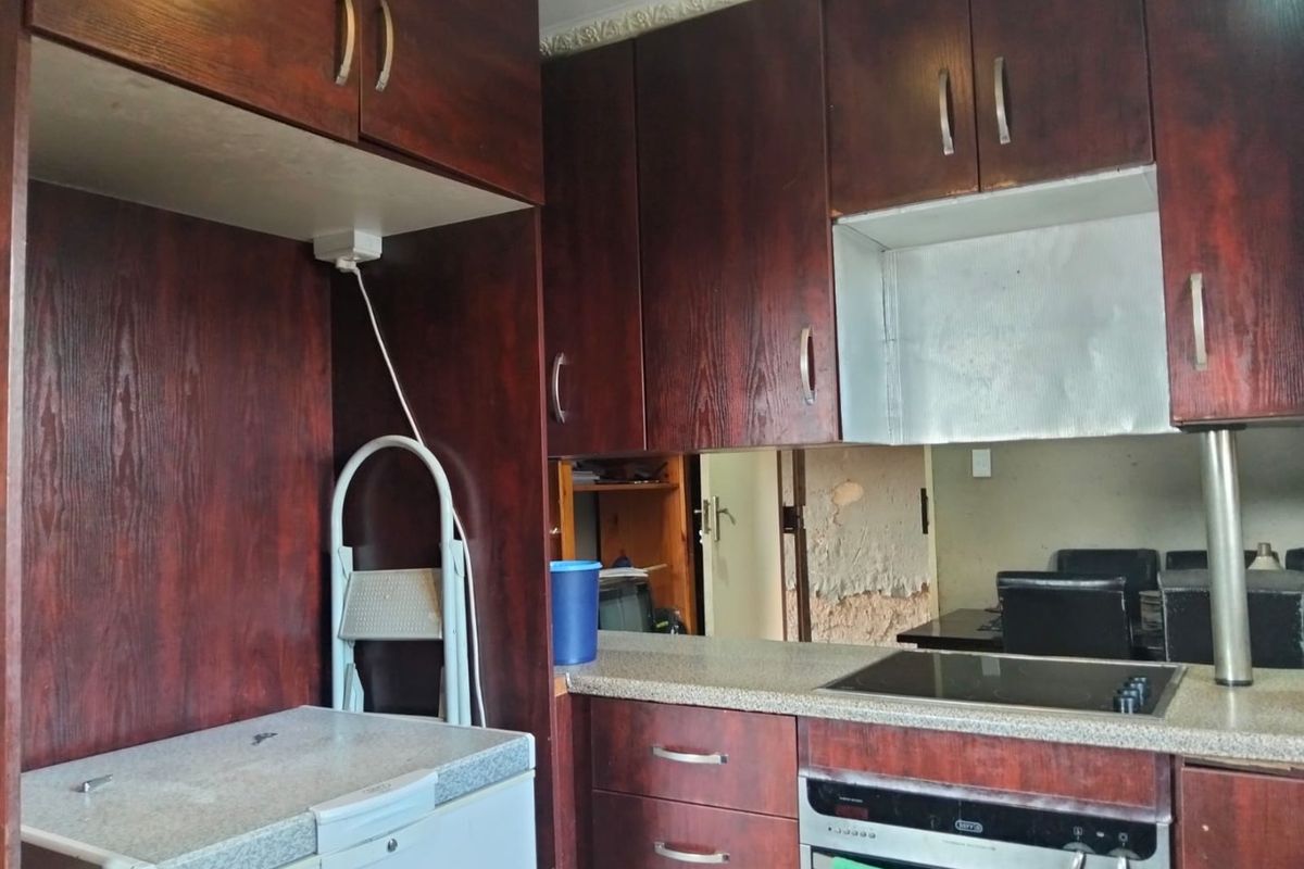Kitchen featuring dark wood-look cabinetry, laminate countertops, and integrated oven and hob, requiring cosmetic updates to wall finishes.