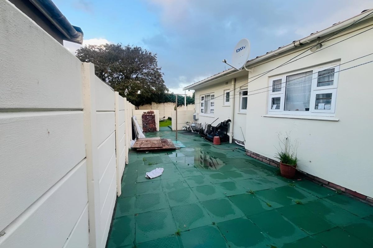 Rear exterior area featuring a paved patio, precast boundary wall, and external utility access points, currently showing signs of poor drainage and maintenance.