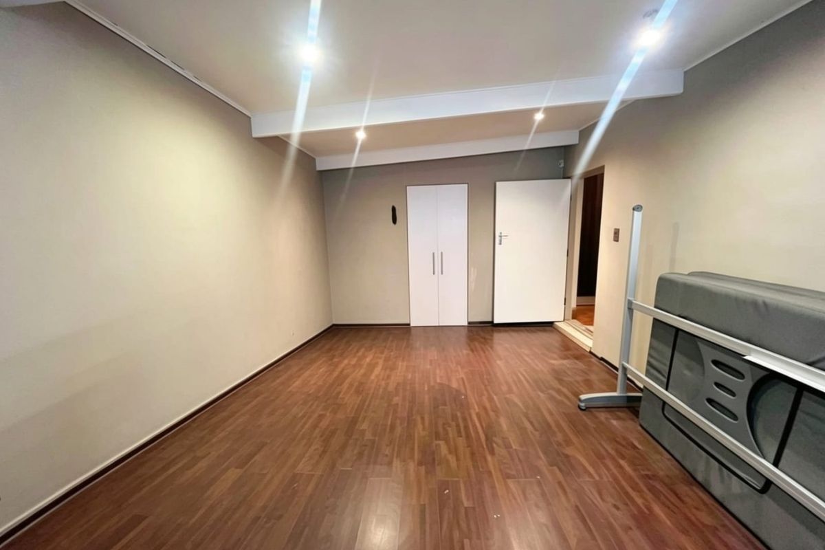 A spacious, empty bedroom featuring laminate flooring, neutral walls, and built-in cupboard storage, offering a clean canvas for personalization.