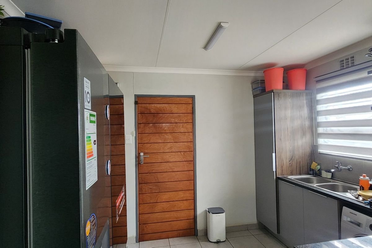 A functional kitchen featuring modern grey cabinetry, stainless steel sink, tiled flooring, and a solid timber door, providing a practical workspace.