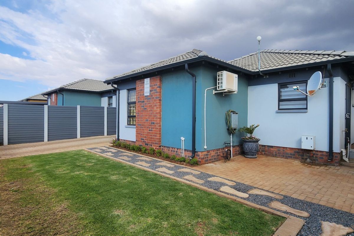 Rear view of the property featuring a paved patio area, landscaped garden, and secure boundary walling.