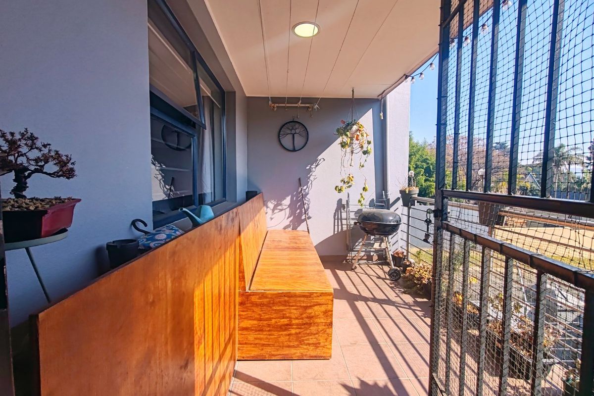 A covered balcony featuring tiled flooring, a built-in wooden bench, and a secure metal gate, offering a functional outdoor space.