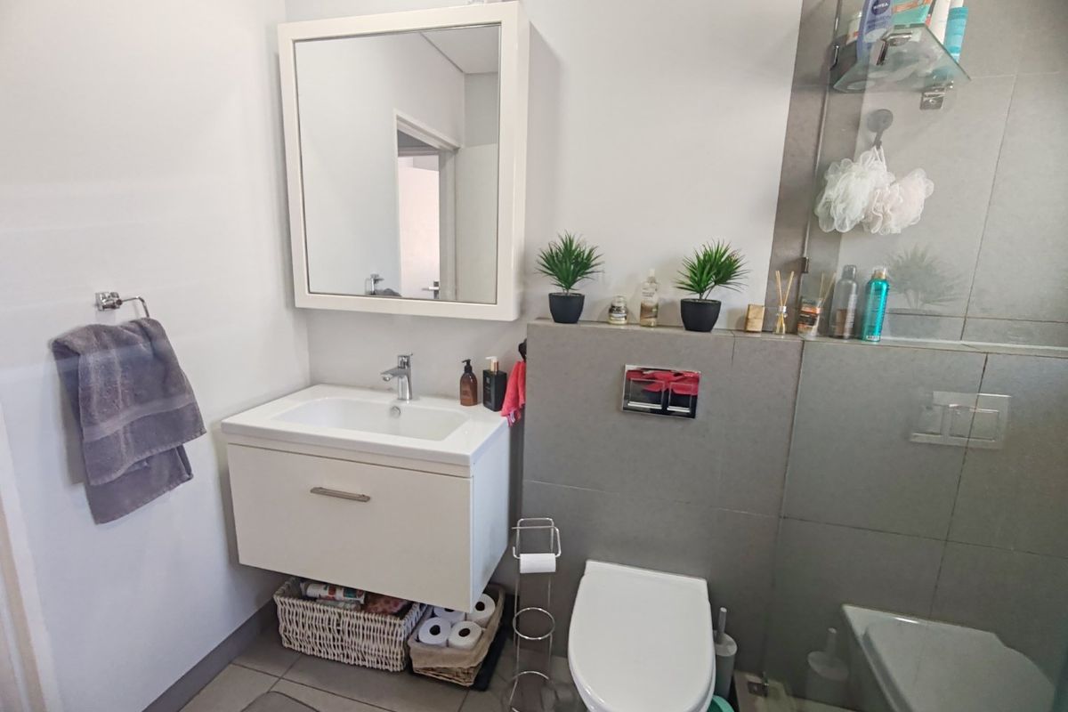 Modern bathroom featuring a wall-mounted vanity, wall-hung toilet with concealed cistern, and a glass-enclosed shower area with neutral tiling.