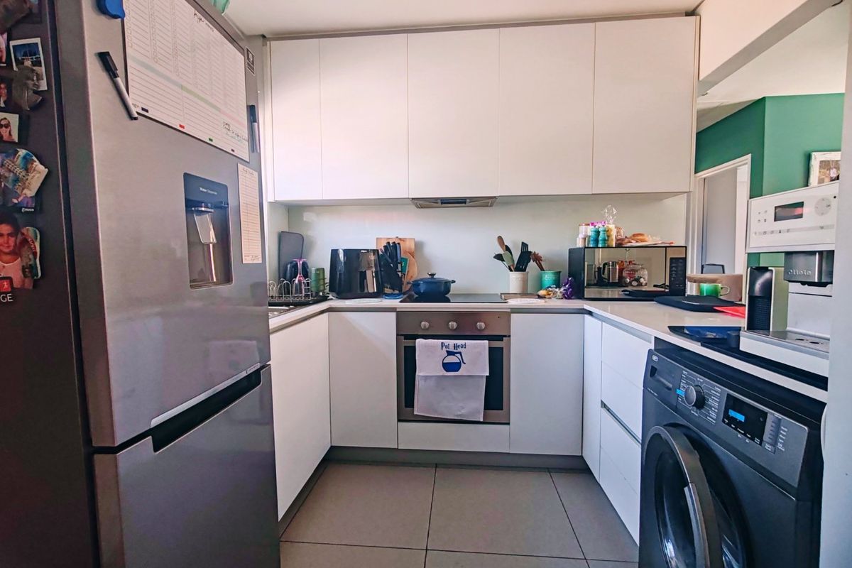 Compact modern kitchen featuring white handleless cabinetry, stone countertops, integrated oven and hob, and tiled flooring.