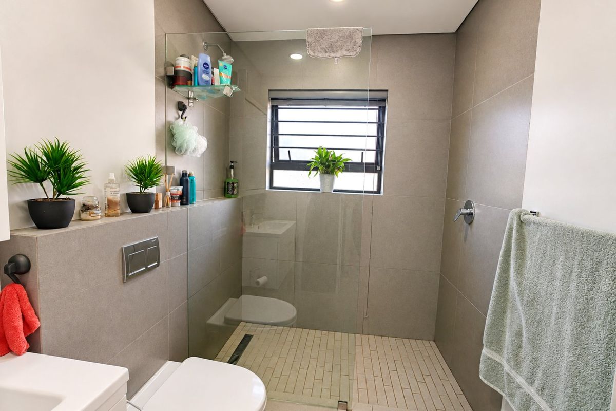 Modern bathroom featuring a walk-in shower with a glass screen, wall-mounted toilet, and neutral large-format wall tiles.