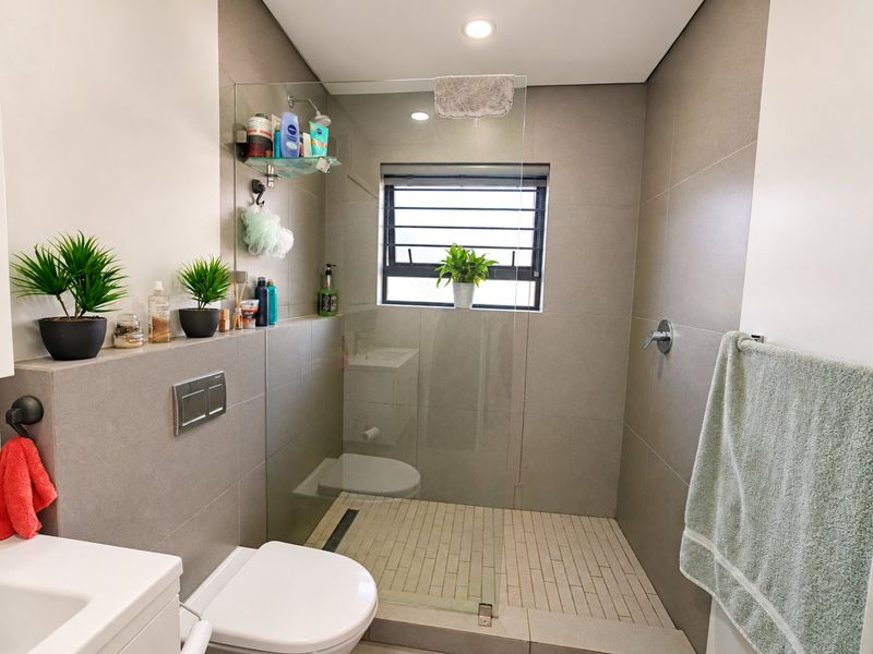 Modern bathroom featuring a walk-in shower with a glass screen, wall-mounted toilet, and neutral large-format wall tiles.