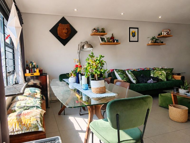 A bright open-plan living and dining area featuring neutral tiled flooring, recessed downlighting, and floating wall shelving.
