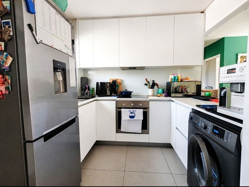 A compact, modern kitchen featuring white cabinetry, integrated appliances, a glass splashback, and neutral floor tiles.