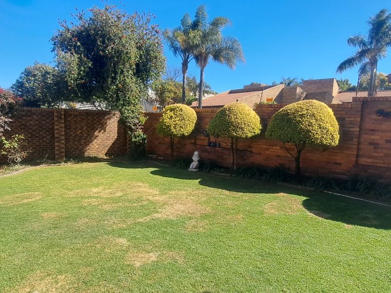 A private rear garden featuring a well-maintained lawn, manicured shrubs, and a brick boundary wall with an adjacent paved patio area.