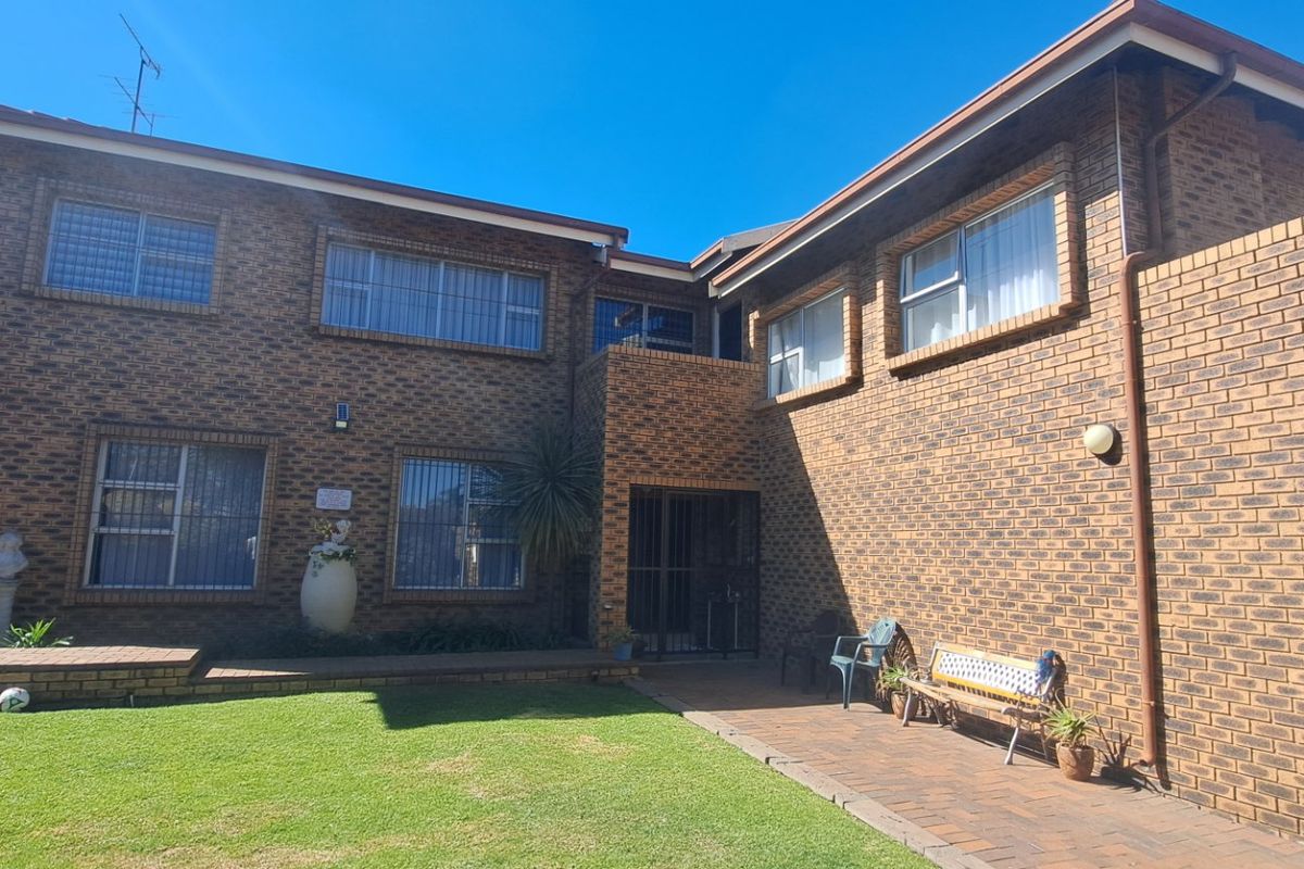 Rear view of a double-story face brick house featuring a paved patio area and a well-maintained lawn.