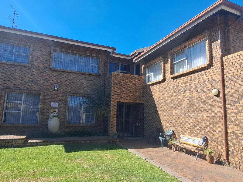 Rear view of a double-story face brick house featuring a paved patio area and a well-maintained lawn.