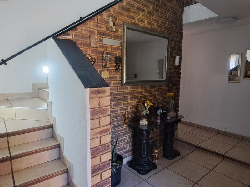 Welcoming entrance hall featuring a tiled staircase with wrought iron handrails and a distinctive exposed brick feature wall.