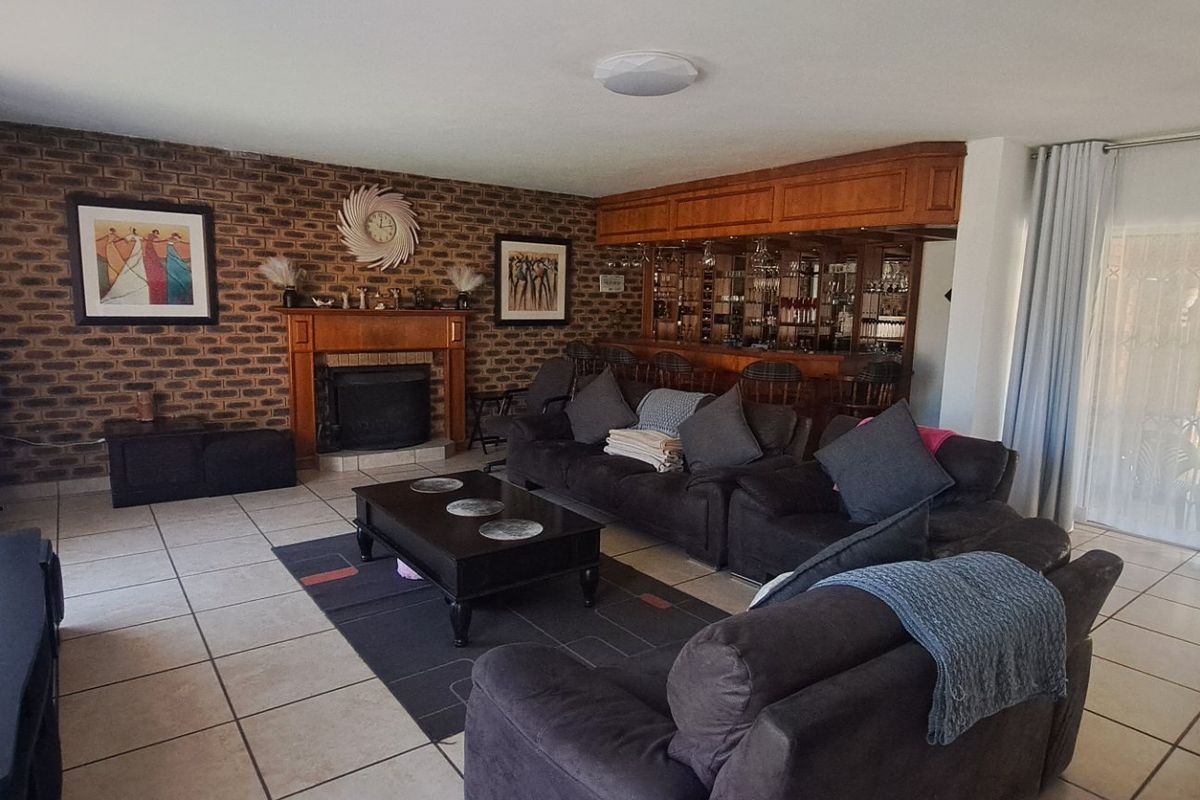 Spacious living room featuring a brick accent wall with a built-in fireplace and a dedicated built-in bar area, finished with neutral floor tiles.