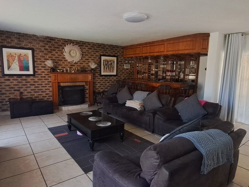 Spacious living room featuring a brick accent wall with a built-in fireplace and a dedicated built-in bar area, finished with neutral floor tiles.