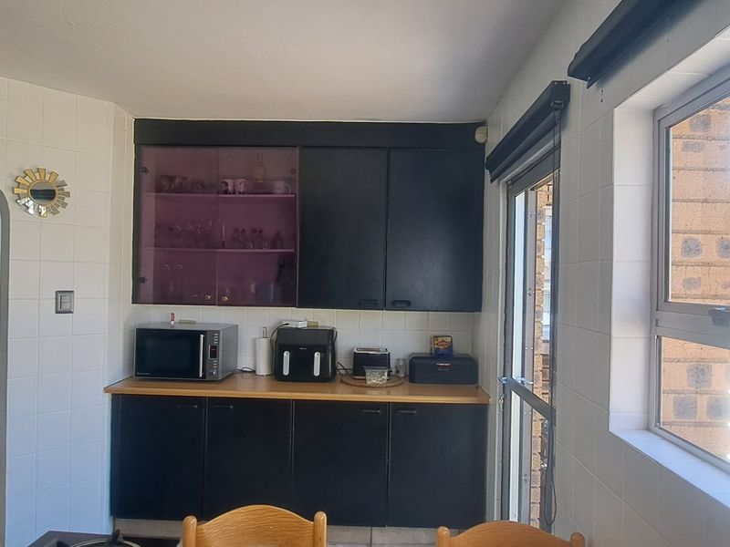 A kitchen area featuring dark built-in cabinetry, tiled walls, and a window with security bars overlooking the exterior.